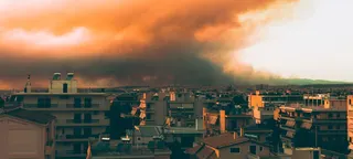 希腊雅典的景色，背景中居民区上空升起由野火产生的大量橙黑色浓烟。
