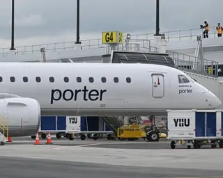 A white Porter Airlines jet is parked at a Montreal airport gate, with ground crew and equipment nearby