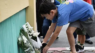 A boy in a blue t-shirt and shorts lays a bouquet of white flowers on the ground.