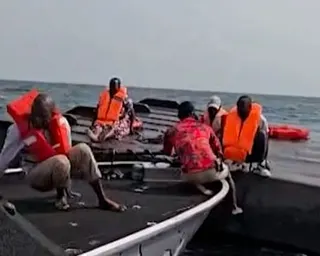 Rescued passengers in life jackets sit atop capsized ferry hull on Lake Kariba.