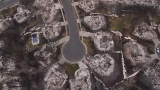 The aerial still shows homes destroyed down to their foundations, with burned cars still parked in some driveways.
