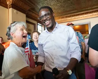 David Crowley smiles, shaking hands with Karen Hilt, who holds an American flag