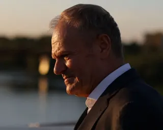 Polish Prime Minister Donald Tusk's face in profile, lit by warm sunset light near a river