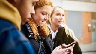Three teenagers standing outside and looking at one phone