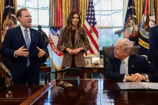 US President Donald Trump sits while Andrew Giuliani, head of the White House Task Force for the FIFA World Cup 2026, and US Homeland Security Secretary Kristi Noem stand by his side.