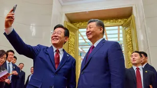 Lee Jae Myung and Xi, both wearing navy suits and red ties, taking a selfie together.