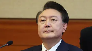 Yoon Suk Yeol sitting in front of a microphone, he is wearing a suit and a red tie