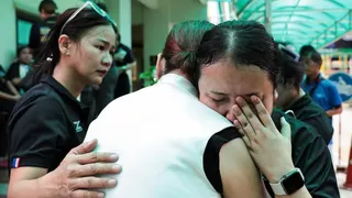Two women hug, with one crying, as another consoles them with a hand on one of their backs