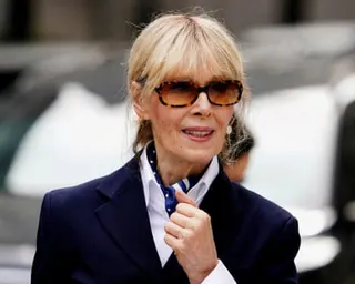 a woman in a blue coat and sunglasses looks off to the side