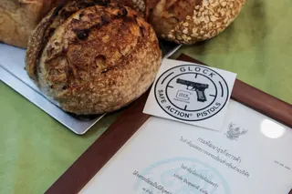 A framed firearms licence and sourdough bread at Suchart and Friends Gun Shop in Bangkok’s historic gun district, where the shop has operated since 1956 and switched to selling sourdough bread before the latest deadly mass shooting because it could no longer import firearms for sale, while continuing to renew its firearm licence each year, as Thailand has suspended firearm purchase permits and announced plans for tougher gun control laws, including a ban on firearm imports and a range of other r