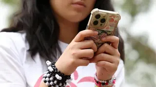 一個戴著彩色手環的少女坐在外面，低頭看著她的iPhone。