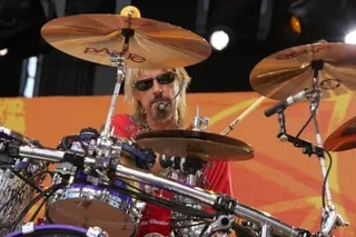 Man in sunglasses and dyed blond hair plays cymbals amid a chrome drum kit onstage