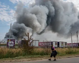 A man walks past a large plume of grey smoke rising from a warehouse