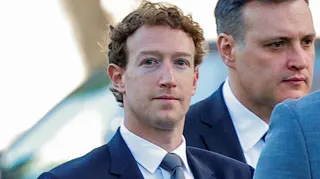 Close up of Mark Zuckerberg wearing a suit, looks towards the camera with a blank expression. He is flanked by staff also in suits. Photographed in February 2026