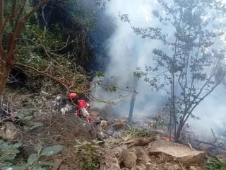 A Kenya Red Cross responder crouches amid smoke and debris near a helicopter crash site