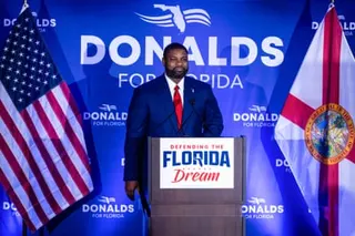 A man stands at a podium with a placard saying 'Defending the Florida Dream' with two US flags at the side.