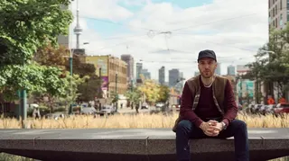 Matteo Sgaramella sits on a concrete slab with the skyline of Toronto in the background