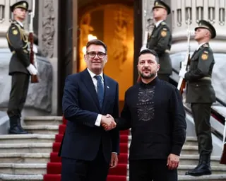 Burnham and Zelenskyy shaking hands in front of an ornate building with a red carpet running up the stairs, and men in military uniform standing guard