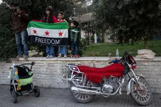 DAMASCUS, SYRIA - DECEMBER 08: People watch soldiers and military vehicles parade through the streets to mark one year since the fall of the Assad regime on December 8, 2025 in Damascus, Syria. The first anniversary of the fall of the Assad regime in Syria is being marked today across the country. Former leader Bashar al-Assad was granted asylum in Russia after he fled the country and his government collapsed on December 8, 2024. The fall of the regime, which ended over five decades of the Assad