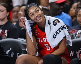 Angel Reese sits on the bench, wiping her face with a towel during a game