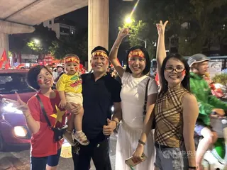 越南民眾金鶯（左1）、阮寧（中）與家人都上街為國家隊26日在東協盃足球賽的勝利慶祝。阮寧開車，車子在機車陣中緩慢前行，他索性把車停在路邊，與路過機車騎士擊掌歡呼。中央社記者曾婷瑄河內攝　115年8月27日