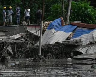 Rescuers in hard hats survey a corrugated metal building lying buckled in flood water
