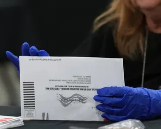 An election worker's gloved hands hold a vote-by-mail ballot envelope