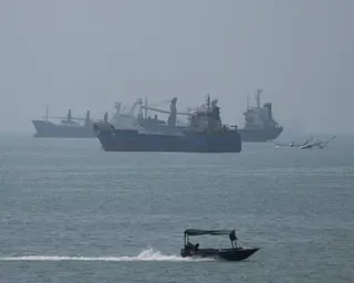 Cargo ships anchored in the strait as a small speedboat passes by