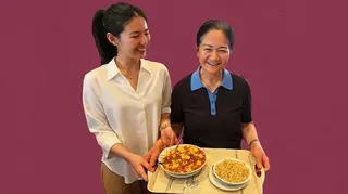 賀灕灑（左）和母親 Sophie（右）身處她們的麗都餐廳。Lisa 正看著母親微笑，母親捧著托盤和菜餚正要上菜。