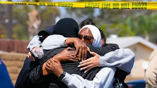 Women wearing hijabs wrap their hands around one another as yellow police caution tape waves above their heads