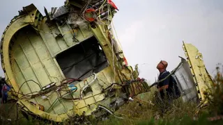 A Malaysian air crash investigator inspects the crash site of Malaysia Airlines Flight MH17 in the Donetsk region of Ukraine in July 2014.  The man is looking at the wreckage of a plane, which has lots of exposed wires.