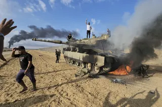 Palestinians celebrate by a destroyed Israeli tank at the Gaza Strip fence on October 7, 2023. Photo: AP