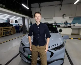 Alex Kendall stood in front of a Wayve car wearing brown chinos and a dark navy blue shirt