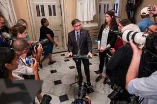 a man speaks into a microphone as people hold cameras and phones in his direction
