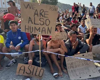 Crowd of people holding placards, one of which reads ‘We are also human’.