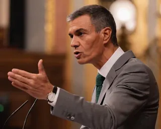 Man in grey suit gestures with hand as he speaks.