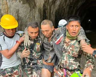 Rescuers on either side of a man support him as he comes out of a tunnel