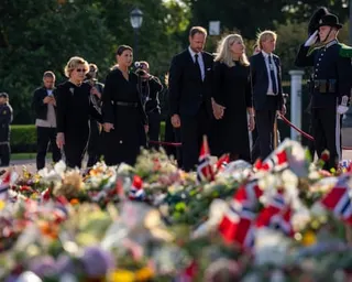 Members of Norway’s royal family seen walking behind a wide spread of flowers and Norwegian flags