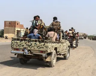 Men ride in pickup trucks along a road